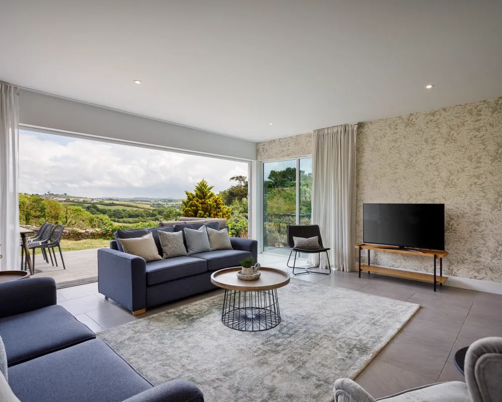 Rolling green Cornish farmland with historic stone farmhouse and coastal views beyond